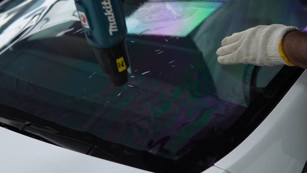 Installer using a heat gun to shape window film on the glass of a Tesla Model Y Performance